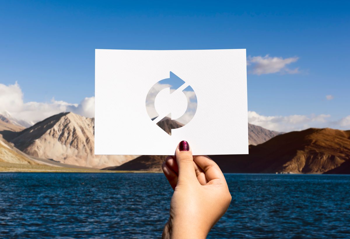 Mano que tiene un papel con el simbolo del Icono de actualización de recarga en un papel perforado, el fondo de la imagen muestra un lago con montañas
